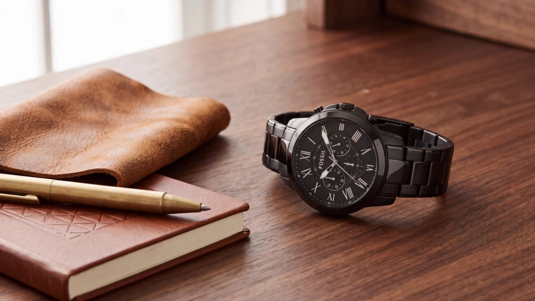Montre Fossil homme Grant à cadran noir et chiffres romains posée sur du cuir et du bois